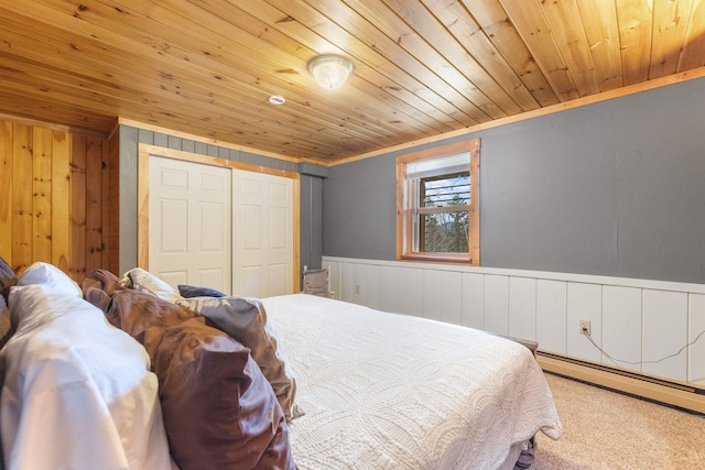 carpeted bedroom featuring ornamental molding, a closet, a baseboard heating unit, wainscoting, and wooden ceiling