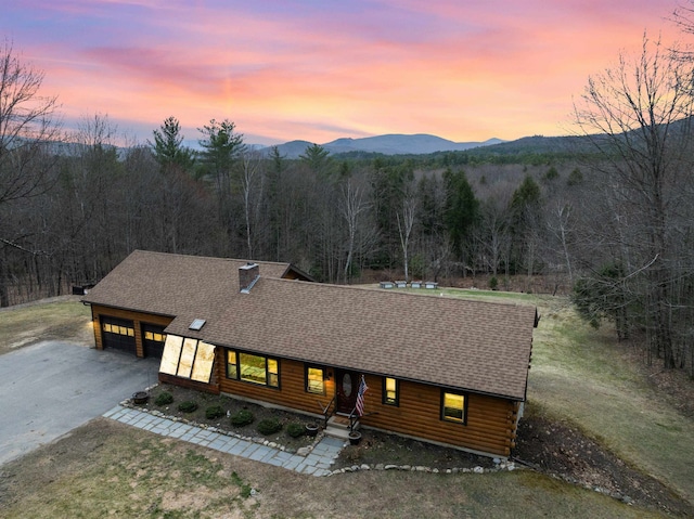 log-style house with log exterior, roof with shingles, a view of trees, driveway, and a mountain view