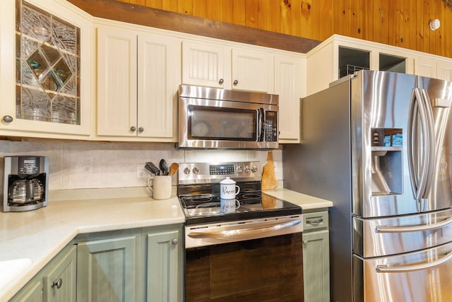 kitchen featuring stainless steel appliances, green cabinets, light countertops, glass insert cabinets, and tasteful backsplash