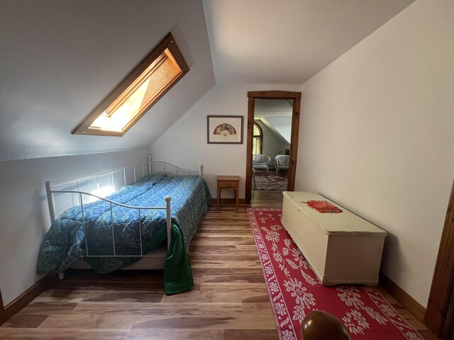 bedroom with vaulted ceiling, wood finished floors, baseboards, and a skylight