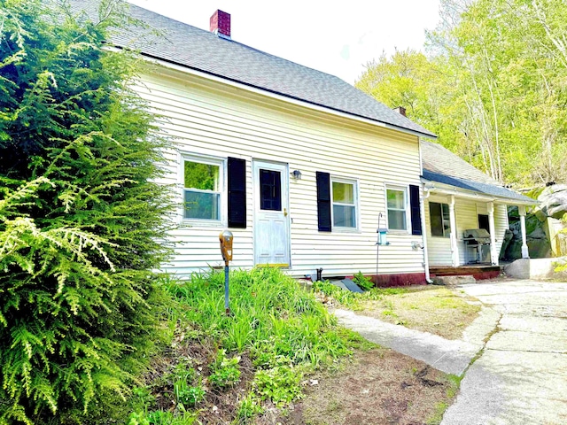 view of front of property featuring a porch, a chimney, and roof with shingles