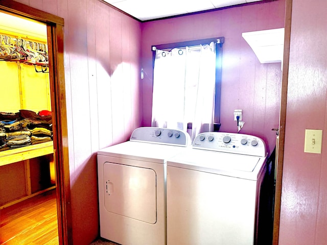 washroom featuring washing machine and clothes dryer, light wood-style floors, and wood walls