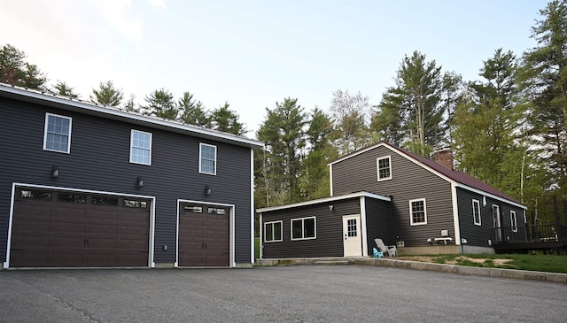 view of front facade featuring an attached garage, a chimney, and driveway