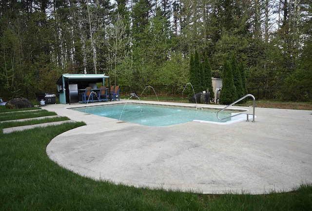 outdoor pool with a patio and a view of trees