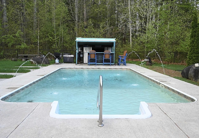 outdoor pool with fence, a patio area, and a view of trees