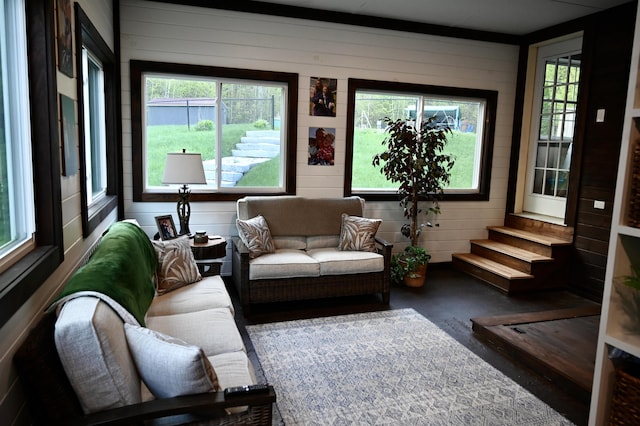 living area with healthy amount of natural light, wooden walls, and stairway