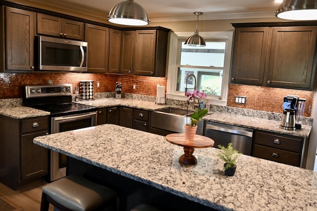 kitchen featuring stainless steel appliances, a breakfast bar, light stone countertops, dark brown cabinets, and a sink