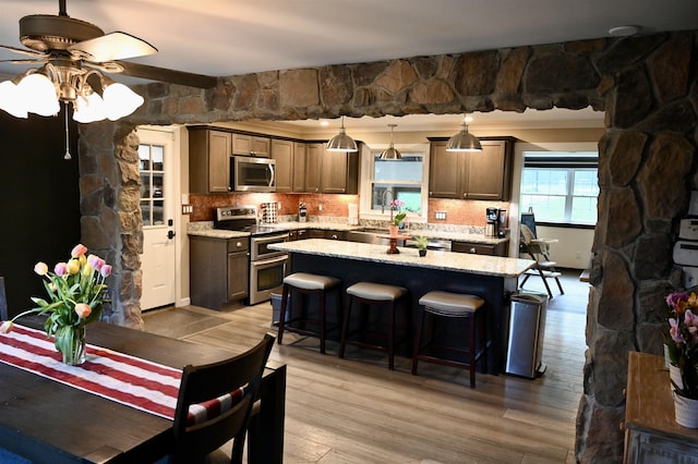 kitchen with appliances with stainless steel finishes, a ceiling fan, decorative backsplash, and a kitchen island
