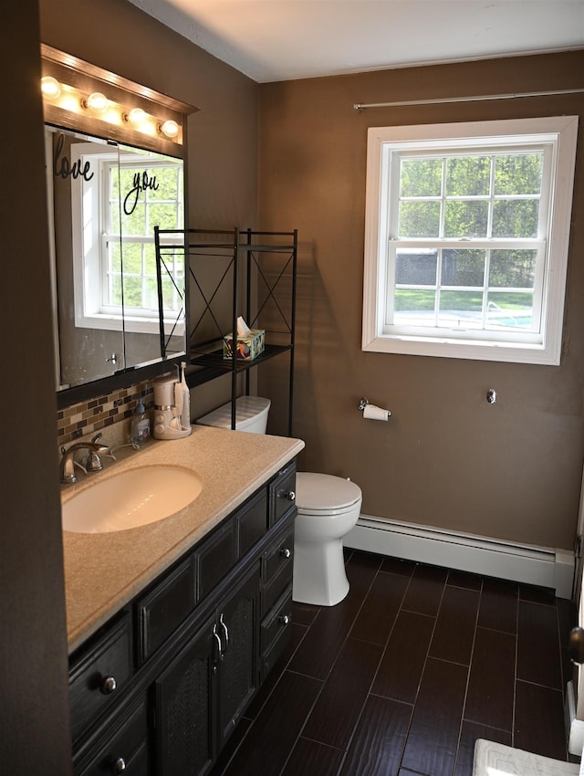 bathroom featuring a baseboard heating unit, vanity, baseboards, toilet, and tasteful backsplash