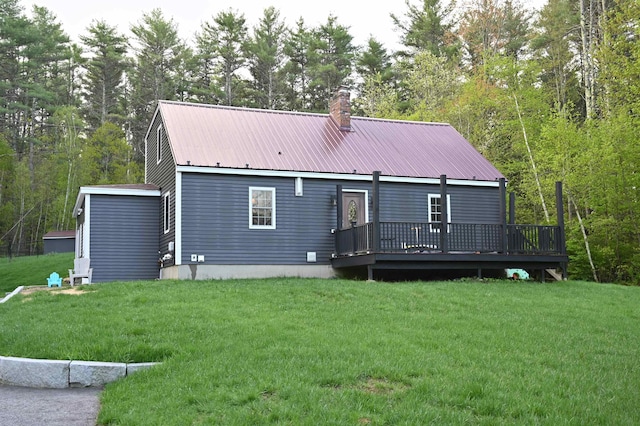 rear view of house featuring a chimney, a wooden deck, a yard, and metal roof