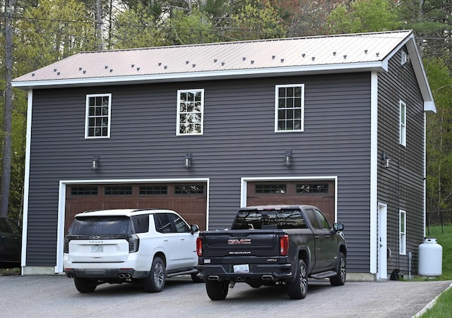 view of front facade with a garage, metal roof, and asphalt driveway