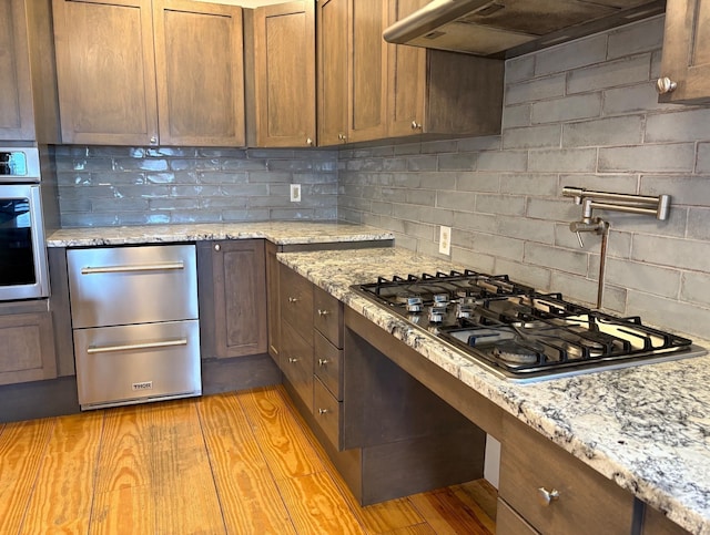 1202 Cotton Rd, Lyndon, VT 05851 - kitchen featuring under cabinet range hood, stainless steel appliances, tasteful backsplash, light stone counters, and a warming drawer