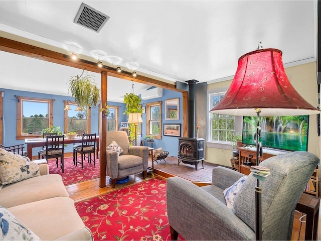 living area featuring a wood stove, a wall mounted air conditioner, and wood finished floors