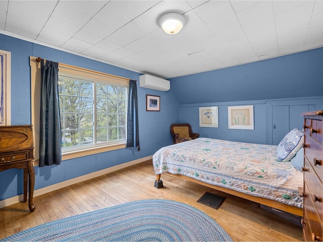 bedroom with an AC wall unit, hardwood / wood-style floors, lofted ceiling, and baseboards