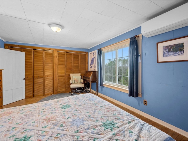 bedroom with a wall mounted AC, wood finished floors, and baseboards