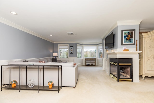 living room with crown molding, a glass covered fireplace, wainscoting, carpet flooring, and a decorative wall