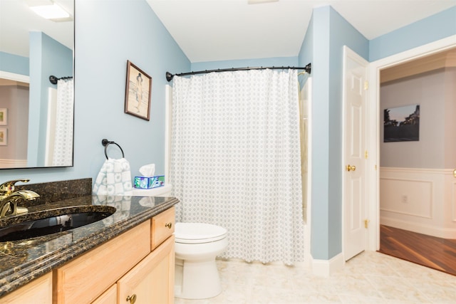 bathroom with toilet, vanity, a shower with shower curtain, and a wainscoted wall