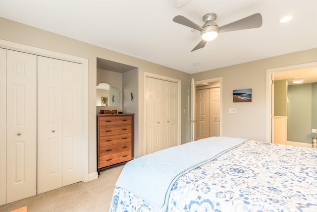 bedroom with two closets, light carpet, and a ceiling fan