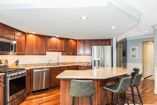 kitchen with stainless steel appliances, wood finished floors, a breakfast bar, light stone countertops, and wainscoting