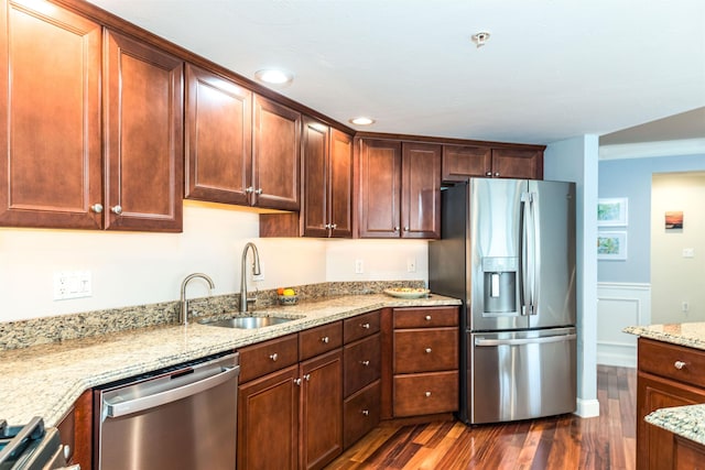 kitchen featuring stainless steel appliances, a sink, dark wood-type flooring, light stone countertops, and a wainscoted wall