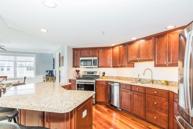 kitchen with stainless steel appliances, a sink, light wood finished floors, light stone countertops, and a kitchen bar