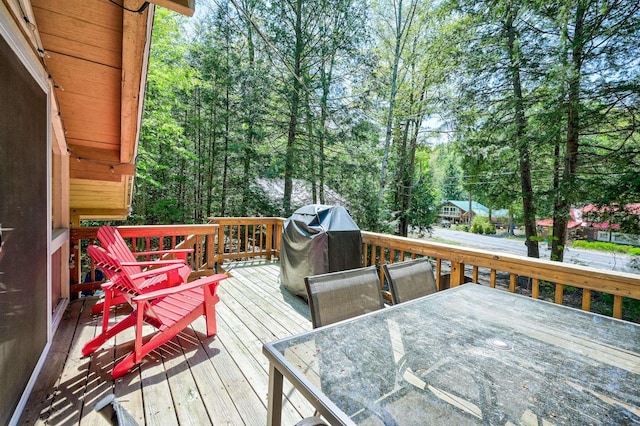 wooden terrace featuring area for grilling, outdoor dining space, and view of scattered trees