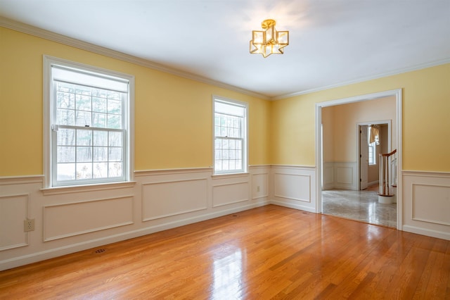 spare room featuring wainscoting, a chandelier, light wood-style floors, crown molding, and a decorative wall
