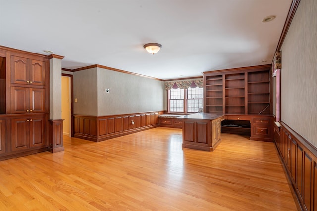 unfurnished office with light wood finished floors, crown molding, a wainscoted wall, and built in study area