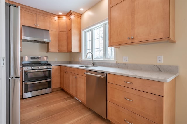 kitchen with stainless steel appliances, under cabinet range hood, a sink, light wood-type flooring, and light brown cabinets