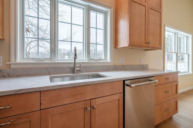 kitchen featuring dishwasher, a sink, light stone counters, light wood-type flooring, and light brown cabinets