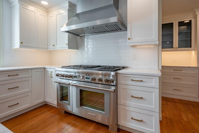 kitchen with range with two ovens, wall chimney range hood, light wood-style flooring, and tasteful backsplash