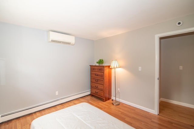 bedroom with a baseboard heating unit, a wall mounted air conditioner, light wood-style flooring, and baseboards