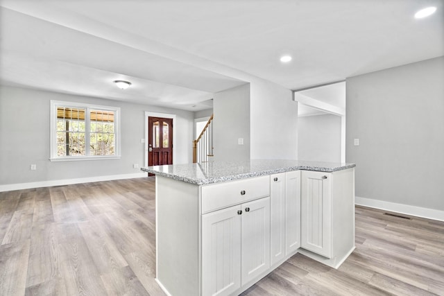 kitchen featuring light stone countertops, light wood finished floors, a kitchen island, baseboards, and recessed lighting