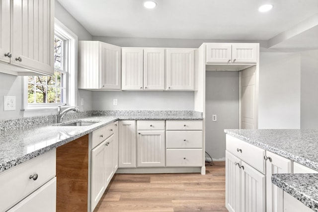 kitchen featuring a sink, light wood finished floors, white cabinets, recessed lighting, and light stone countertops