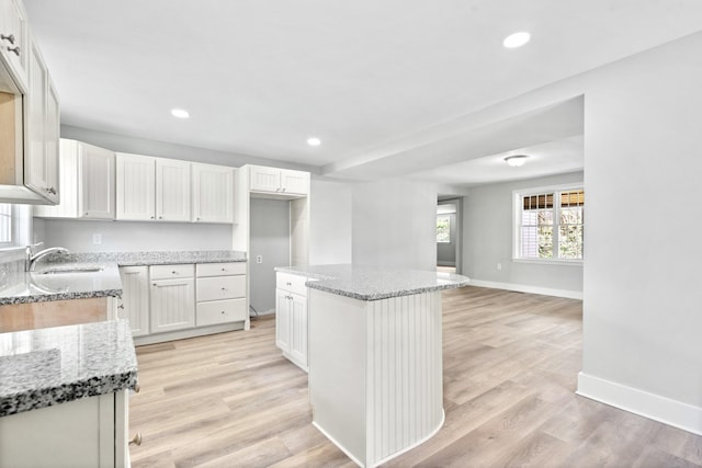 kitchen with a sink, baseboards, a kitchen island, light stone countertops, and recessed lighting
