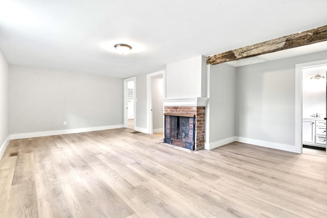 unfurnished living room with light wood-style flooring, a brick fireplace, and baseboards
