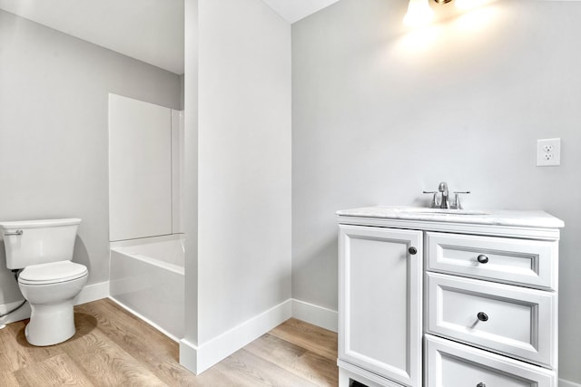bathroom featuring wood finished floors, toilet, vanity, baseboards, and bathing tub / shower combination