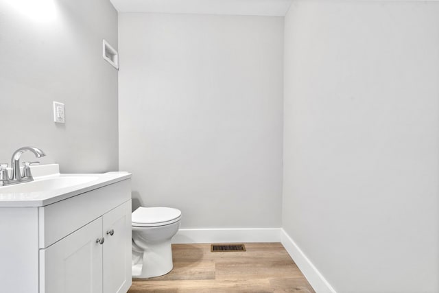 half bath with wood finished floors, vanity, toilet, and baseboards