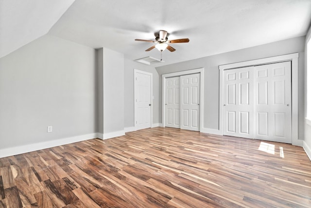 unfurnished bedroom featuring wood finished floors, multiple closets, baseboards, a ceiling fan, and lofted ceiling