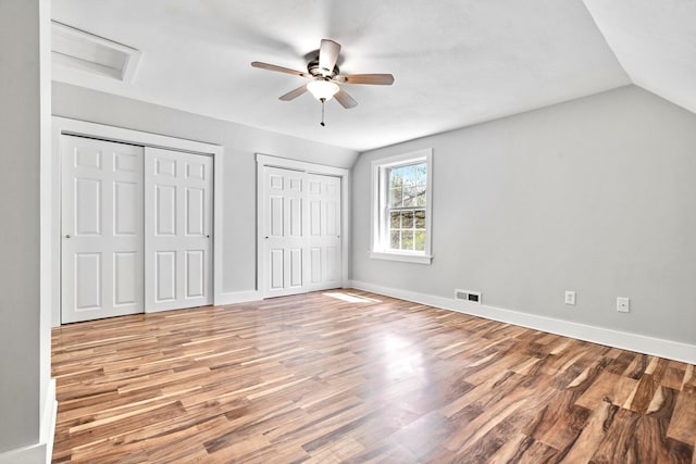 unfurnished bedroom featuring multiple closets, wood finished floors, vaulted ceiling, baseboards, and ceiling fan