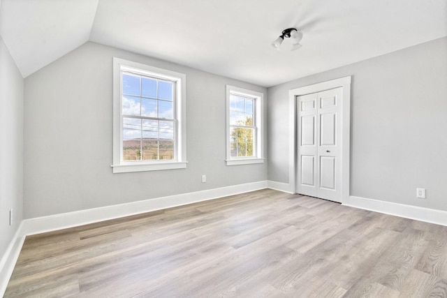 unfurnished bedroom with vaulted ceiling, wood finished floors, a closet, and baseboards