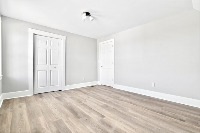 unfurnished bedroom featuring light wood-style floors, baseboards, and a closet