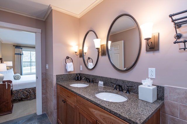 ensuite bathroom featuring crown molding, tile walls, a wainscoted wall, double vanity, and tile patterned flooring