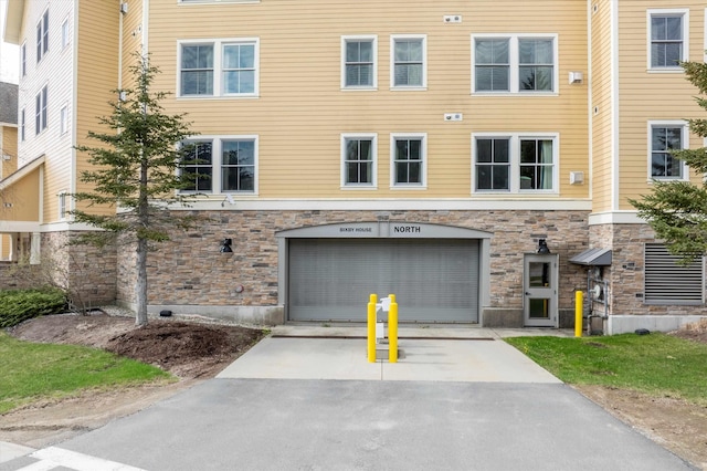 view of property featuring stone siding, an attached garage, and driveway