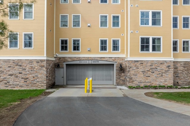 view of front of house featuring stone siding, asphalt driveway, and a garage