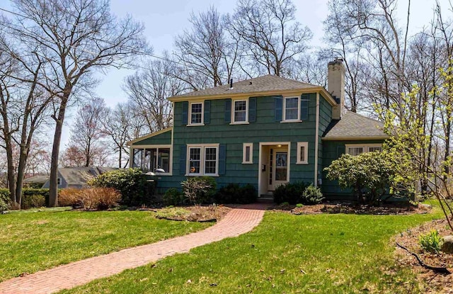 colonial-style house with a chimney, a front lawn, and roof with shingles
