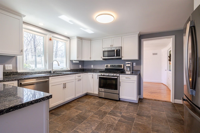 kitchen with appliances with stainless steel finishes, a sink, white cabinets, dark stone counters, and baseboards
