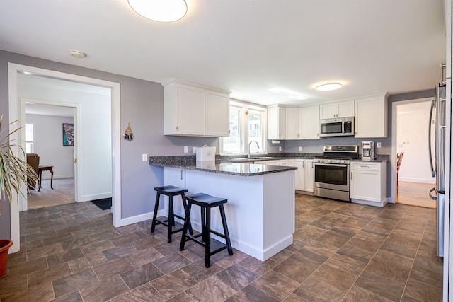 kitchen with stainless steel appliances, a peninsula, white cabinets, baseboards, and dark stone countertops