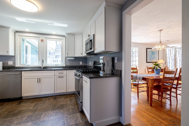 kitchen with appliances with stainless steel finishes, a chandelier, a sink, white cabinets, and dark stone counters