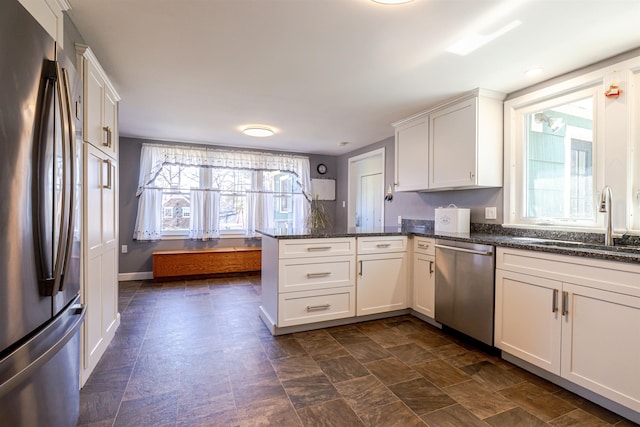 kitchen featuring appliances with stainless steel finishes, a peninsula, a sink, white cabinetry, and dark stone countertops